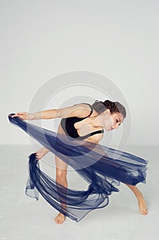 A slender gymnast in black tights dances with a blue chiffon that develops.Aesthetics of dance