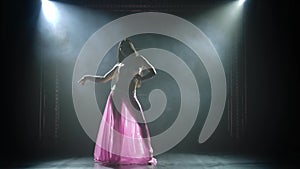 Slender high oriental dancer is dancing on a black background in the smoke. Silhouette of a young woman in an oriental