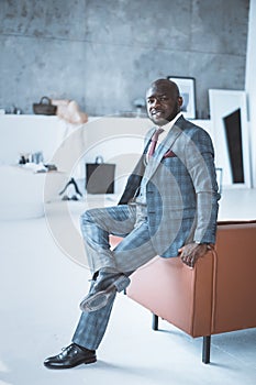 Slender Man in a Plaid Gray Business Suit Sits on the Arm of Couch in his Futuristic Office. Stylish PR Manager is Ready
