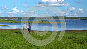 A slender man and woman walk along the shore holding hands.