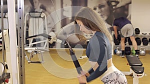 A slender strong girl trains a triceps in a crossover in the gym.