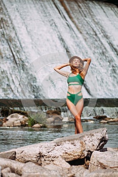 A slender sweet girl stands against the backdrop of a picturesque waterfall