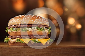 Slender tall double burger with meat and cheese on a wooden table with bokeh on the background