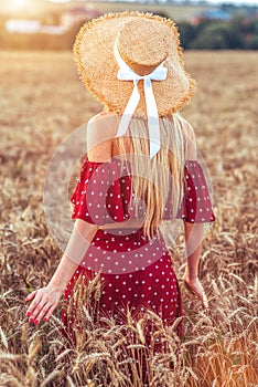 Slender tanned girl in red dress, woman walks wheat field. Summer weekend in village, healthy lifestyle. Walk in fresh