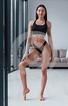 Slender woman in black fitness underwear standing indoors in room at daytime