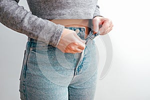 A slender woman fastens a button of her blue jeans. Weight ungain woman getting dressed wearing jeans. Close up of girl buttoning
