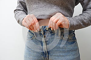 A slender woman fastens a button of her blue jeans. Weight ungain woman getting dressed wearing jeans. Close up of girl buttoning