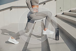 Slender woman in gray sportswear doing exercises outdoors on stair, forward lunges