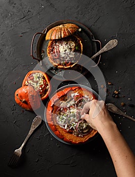 Slender woman hand pouring grated cheese on pumpkin stuffed with rice, mushrooms and onions and smaller pumpkins with red rice and