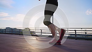 slender woman is jogging alone in early morning in city in summer day, closeup of female legs