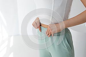 Slender woman measuring her slim waist. dressed in green sportswear. on a white background