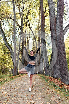 Slender woman performs vrikshasana exercise, tree pose with arms raised and spread to the sides