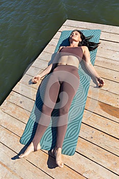A slender woman practicing yoga, doing a relaxing shavasana exercise after the main workout, lies in sportswear on a mat near the