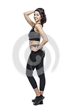 A slender woman in sportswear does exercises. Beautiful brunette in black leggings and top. Health, sports and slimness. Full