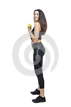 A slender woman in sportswear with green dumbbells does exercises. Beautiful smiling brunette in a black top and leggings.