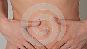 Slender woman touches her naked belly, close-up.