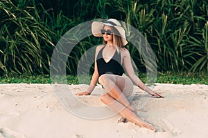 Slender young beautiful girl in black body posing on the beach, wearing a fashionable hat with wide brim, enjoying
