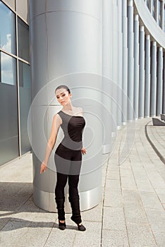 Slender young graceful ballerina standing near the column of the building