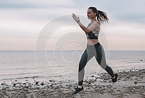 Slender young woman runs along the seashore at sunset, runner