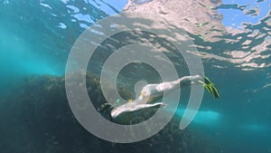 A slender young woman swims in a scuba mask and snorkel underwater in a transparent sea with a sandy bottom