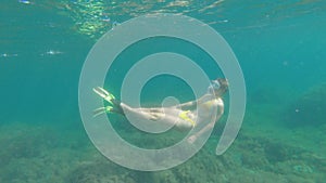 A slender young woman swims in a scuba mask and snorkel underwater in a transparent sea with a sandy bottom