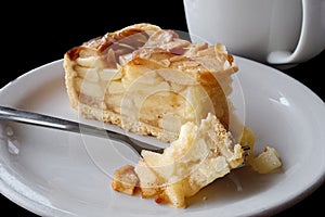 A slice of apple pie with pie on fork on white ceramic plate next to a fork. Black background.