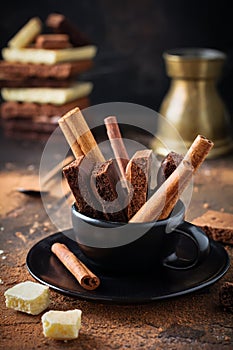 Slice of bitter, milky, porous, airy chocolate and cinnamon in black ceramic cup over dark old background