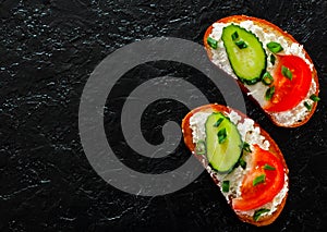 Slice of bread with cream cheese, cucumber, tomato on a black stone board. with copy space. top view