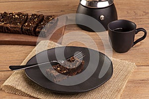 A slice of brownie on a plate with a cup of coffee on wooden table