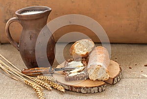 A slice of buttered bread on a wooden board, a crock of milk and mature ears