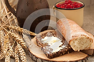 A slice of buttered bread on a wooden board, a crock of milk, a metal cup of red currants and mature ears