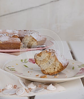 Slice of cake Ciambellone with crumbs on ceramic plate painted with floral motifs, cloth towel and mother of pearl fragments.