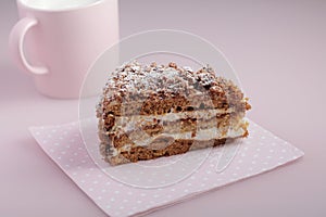 Slice of cake with icing on pink background and pink cup of milk