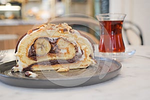 A slice of cake on serveware next to a glass of tea drinkware