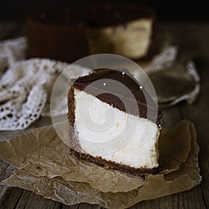 Slice of cheesecake with chocolate on plate, still life with a rustic brown background. Close up, copy space.