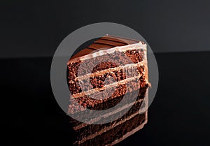 Slice of chocolate cake on a reflective surface minimalist black background