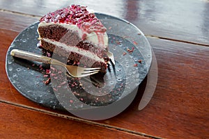 Slice of chocolate and white cream cake with raspberry sauce and decorate by dry rose petal on top of cake and black plate