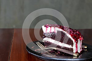 Slice of chocolate and white cream cake with raspberry sauce and decorate by dry rose petal on top of cake and black plate