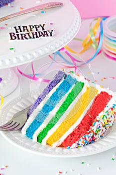 A slice of decorated rainbow birthday cake, ready to be eaten.