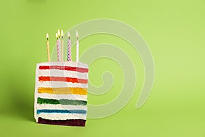 Slice of delicious rainbow cake with candles on color background