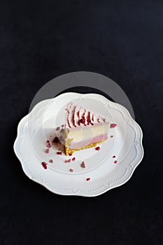 A slice of delicious raspberry cheesecake decorated with freeze-dried raspberries on a white plate stands on a dark background,