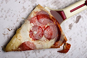 Slice of fresh Italian classic original Pepperoni Pizza and pizza cutter on grease stains white cardboard.