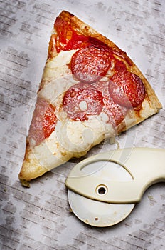 Slice of fresh Italian classic original Pepperoni Pizza and pizza cutter on grease stains white cardboard.