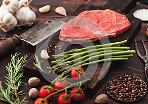 Slice of fresh raw barbeque braising beef steak on chopping board with asparagus and garlic with tomatoes and salt with pepper on