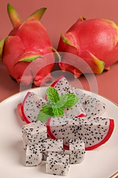 Dragon fruit with mint on white plate for dessert on pink background, closeup