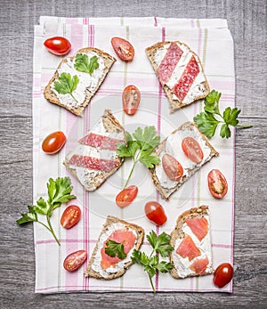 Slice of fresh rye bread with cream cheese with red fish, cherry tomatoes and salami parsley on a striped tablecloth on w