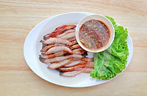 Slice grilled pork served with spicy sauce on white plate on wood table background, thai style food