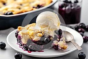 Slice of home baked delicious blueberry crumble with a scoop of vanilla ice cream on a plate with juicy jammy berry filling