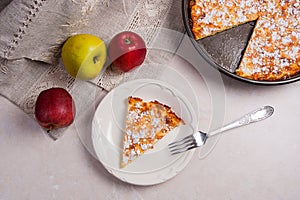 Slice of homemade apple pie with fork and fresh apples on light