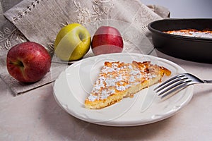 Slice of homemade apple pie with fork and fresh apples on light